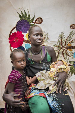 Angelina Nyanuba (25) with her children Mary Nyakir (3) and Omar Basir (two months) in front of her Milaya (a traditional hand-decorated sheet) in the Bidibidi refugee settlement. "My husband was a so...