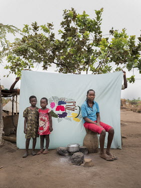 Viola Desire (19) from Yei in South Sudan sitting in front of her Milaya (a traditional hand-decorated bedsheet) with her nieces Christine Kiden (5) and Betty Nyoka (4) in Bidibidi refugee setttlement...