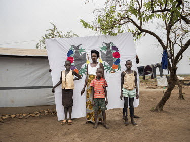 Mary Kiden and her children in front of a Milaya (a traditional hand-decorated bedsheet) she made. L-R: Christine Nyoka (8), Mary Kiden (26), Mukaya Emmanuel Zobonga (6), Grace Melly (11). Mary and he...
