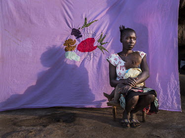 Esther Pond (19) with her daughter Emmason Gift (7 months) seated in front of a Milaya (a traditional hand-decorated sheet) she made.  "In South Sudan people came at night, knocking doors and asking...