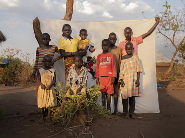 Lucia Goro (37) with her children, nephews and nieces who she is taking care of, standing in front of her Milaya (a traditional hand-decorated sheet) in the Bidibidi refugee settlement. "I got sick th...