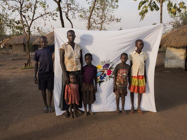 Agnes Tabu (35) standing in front of her Milaya (a traditional hand-decorated sheet) in the Bidibidi refugee settlement with her children Norbert, Emilia, Josephine, Sara and Charity. "In 2016 my brot...