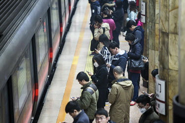 Commuters check their mobile phones as they stand on a subway platform waiting for a train.