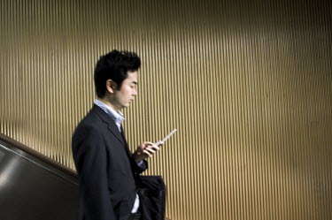 A 'salaryman' checks his mobile phone as he descends by escalator into a metro station.