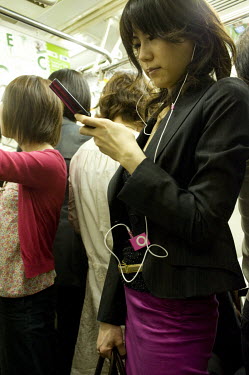 A woman listens to an iPod and checks her mobile while travelling on a metro train.