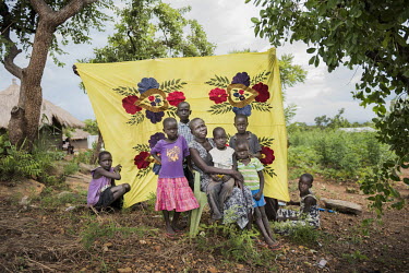Rebecca Ameri (75) from Jonglei State in front of her Milaya (a traditional hand-decorated sheet) in the Bidibidi refugee settlement with her grandchildren Arag Amayen (8), Aney Ayuen (5), Ayuen Ayang...