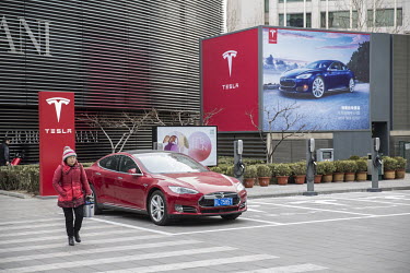 A woman walks past a Tesla Model S parked outside of a Tesla dealership.