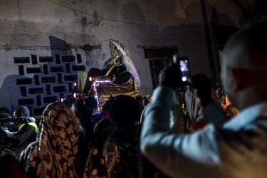 Dhinourayni Ali Kassim Ali Mbaliya wears a ceremonial veil and sword as he is carried through the medina of Domoni on the eve of his wedding. He is accompanied by drummers and followed by a procession...