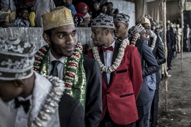 A group of male guests, wearing ceremonial scarves and garlands of flowers, perform a traditional dance during the 'Hambarousi', one of the many events that take place during a traditional wedding.