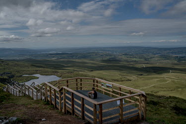 A man looks out over the landscape from a viewing point on Cuilcagh mountain. The UK - Ireland border runs along the top of the mountain.