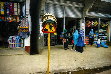 A sign indicates construction work on a street in the suburbs of the citywhere a group of young women chat outside shop a shop selling crafts.