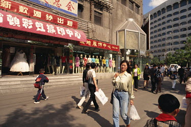 People passing a row of clothing stores on a busy street.