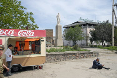 A beggar near a Coca Cola stand and a Lenin monument.