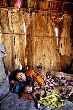 A woman with her baby lie in bed inside a house in the village of Kirindy. The building is constructed from the wood and bark of the baobab (Adansonia Grandidieri) tree.