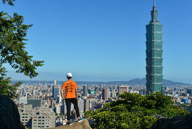 A man stands on Four Beasts Mountain overlooking the city and the prominent Taipei101 Tower.