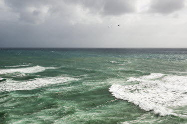 Two helicopters fly over a stormy Mediterranean Sea.
