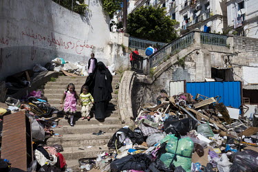 A woman walks with two children down a stairway in the Casbah area heaped with rubbish. The graffiti on the wall reads: 'It's forbidden to throw stones'.