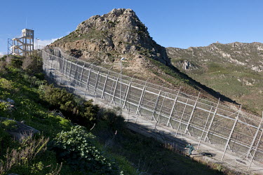 An officer from the Guardia Civil checks the border fence that separates the Spanish territory of Ceuta from Morocco. The rocks in the background are on Moroccan territory. The fence, called 'La Valla...