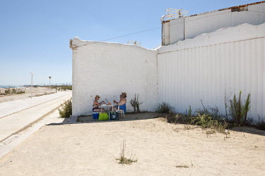 A couple having a picnic in a small stretch of a building's shadow on the Mediterranean coast.