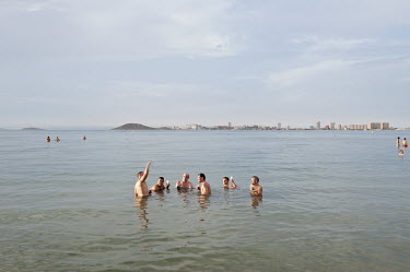 A group of men having a drink in the sea. In the background is the skyline of La Manga del Mar Menor on the Mediterranean coast.