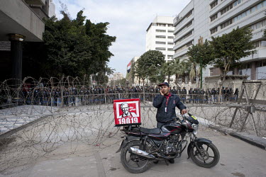 A KFC delivery driver makes a phone call as he stands in front of a barricade of barbed wire, errected by the police to protect the Ministry of Interior from demonstrators.