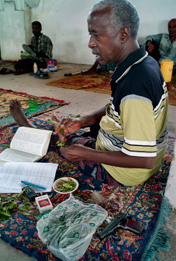 Olat, chewing khat, as he does each afternoon, while reading and taking notes. After the killing of a friend he now carries a pistol with him as protection.