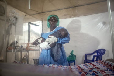 A medical worker who has formerly recovered from Ebola virus and thus can work without the cumbersome personal protective equipment (PPE), holding a child patient inside an a plastic Ebola treatment c...