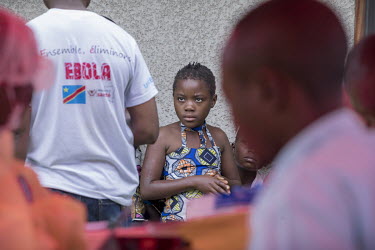 A young girl waits while an Ebola response team prepare their medical equipment during a round of so-called 'ring vaccination', where only people most liable to infection are vaccinated.