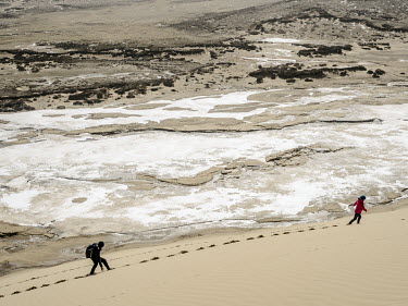 Members of an expedition led by Yang Yong  (geologist, environmentalist and the director of the Hengduan Mountain Research Institute) walk through sand on the edge of a desert overlooking an icy Chac...