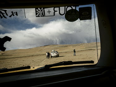 Approaching rain clouds in the desert are seen through a car window as the expedition team reaches a campsite near Rigecuo River, a subsidiary of the Yellow River. In the distance animals graze on the...