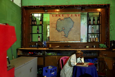 A woman writes at a table, while seated beneath a map of Lake Tana, in a hotel in the port city of Gogora.