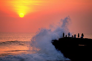 Tourists brave big waves at sunset on the coastline near the Ulu Watu Temple.