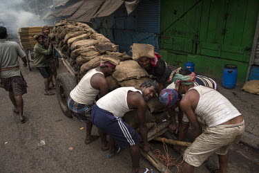 A group of porters prepare to raise a cart, loaded with heavy sacks, onto its wheels.