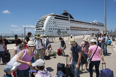 People waiting for a regular ferry boat to the mainland gather with their lugguage near where the MSC Lirica cruise ship is moored during a half day stop.