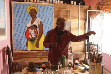 Painter and 'Sapeur' (the French acronym for the Societe des Ambianceurs et des Personnes Elegantes) the Society of Tastemakers and Elegant People, Chéri Samba at work in his studio with one of his p...