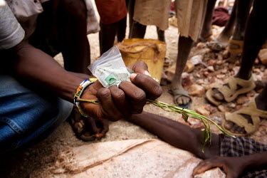 A man at an illegal gold mine holds a bag of gold dust and a stalk of qat.