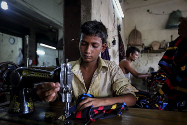 A child worker sews t-shirts in a factory. He works a 12 hour day and is paid less than GBP 20 per month.