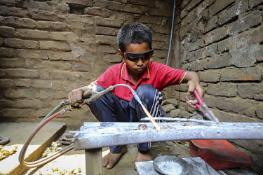 A child uses a welder while working in a factory making door handles and locks.