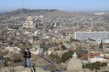 A couple standing on the walls of the Narikala fortress with the city, including the Sameba Cathedral, the biggest cathedral in the Caucasus, laid out below.
