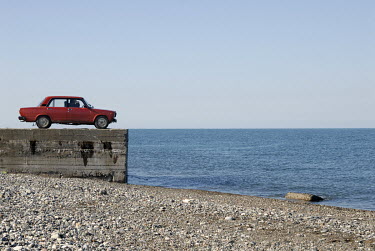 A red Lada parked on the shore of the Black Sea.