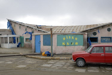 A red Lada waits in front of an old 'Disko Klub' on a Caspian Sea beach.