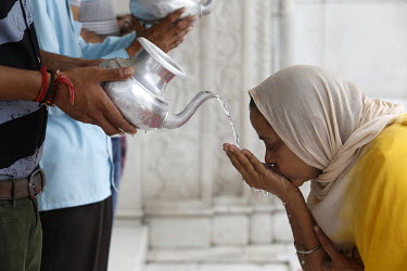 A woman drinks water during a service at the Gurudwara Bangla Sahib.