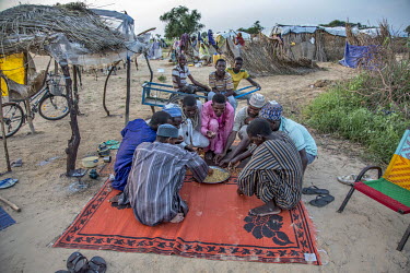 Habu Adamu and other men eating mixed pasta with sauce made by his wife Falmata Adamu. Falmata Adamu and her husband Habu Adamu and children live in an informal IDP camp where Habu does low-paid jobs,...