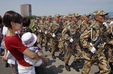 A woman holding a child watches soldiers parade on Abay Square.
