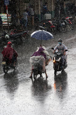 Motor scooters drive along a road through heavy monsoon rainfall.