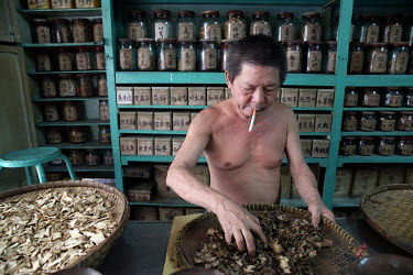 A man smokes while he prepares Chinese medicine at a herbal pharmacy.