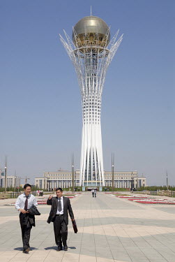 Business men walk past the Bayterek Tower, a monument and observation tower.