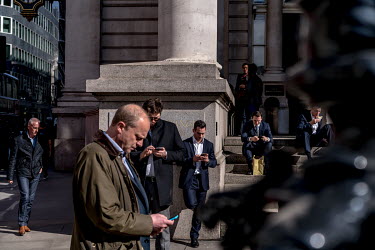 Workers in the City of London check their phones during their lunch hour.