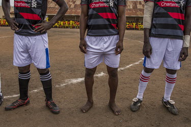 Officials and players, including one playing barefoot, on the pitch for a football match played at Luzira Prison between teams composed of inmates, Liverpool in black versus Manchester United in Red....