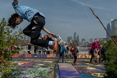 A youth rides a skateboard near people taking part in an Extinction Rebellion protest at Waterloo Bridge.